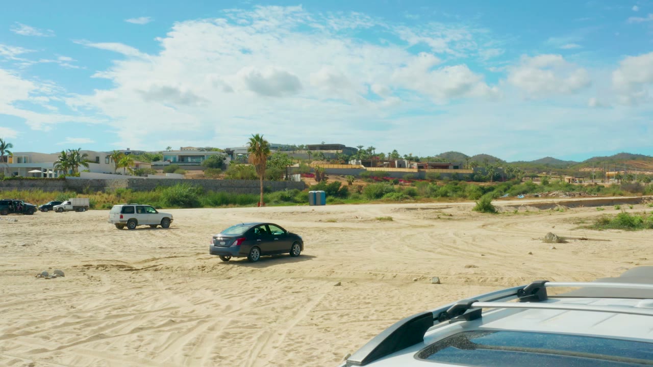 Parked cars on sandy terrain with a vehicle roof entering the foreground.