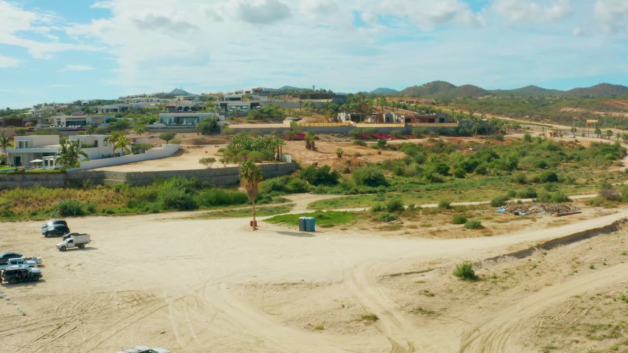 White SUV near the lower edge of a sandy lot with hillside buildings behind it.