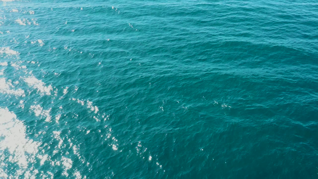 Overhead view of turquoise ocean water at El Tule Los Cabos with bright white foam entering from the left side and no visible people.