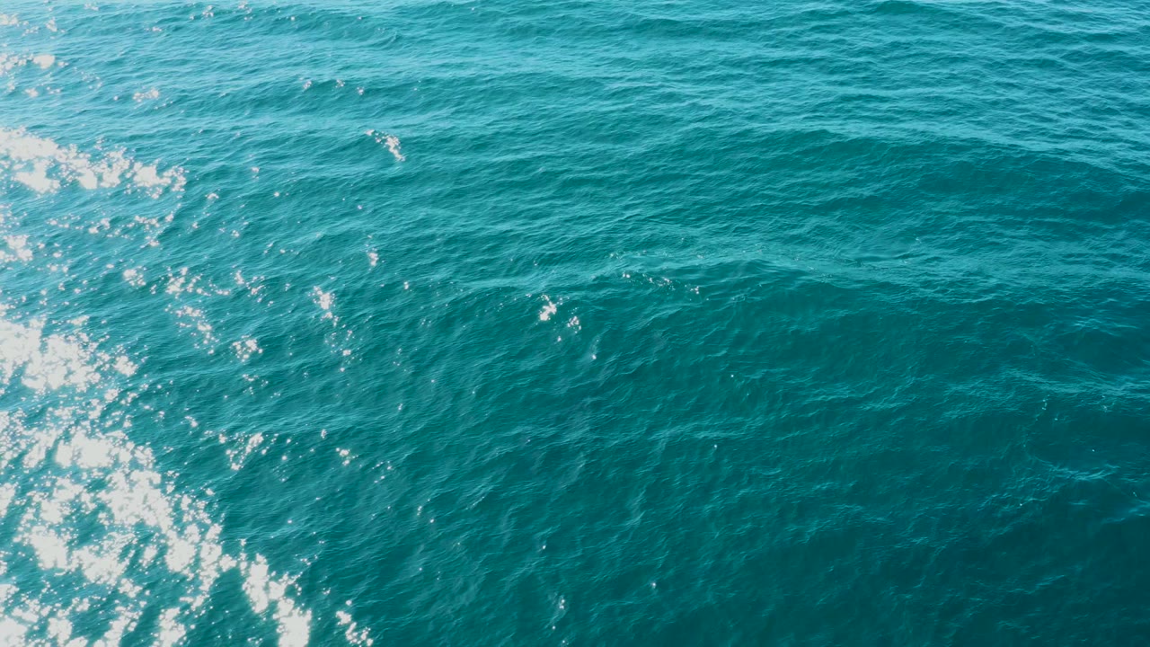 A brighter strip of boat wake foam cuts through turquoise water near the center of the El Tule Los Cabos frame, with no shoreline or visible people.
