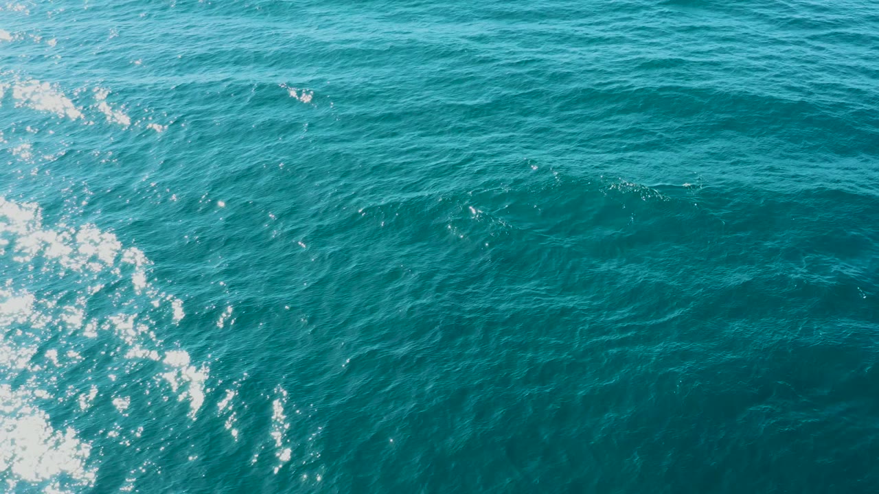 Turquoise water fills the frame while a broken white wake line and sparkling highlights sit left of center, with no visible people in the El Tule Los Cabos shot.