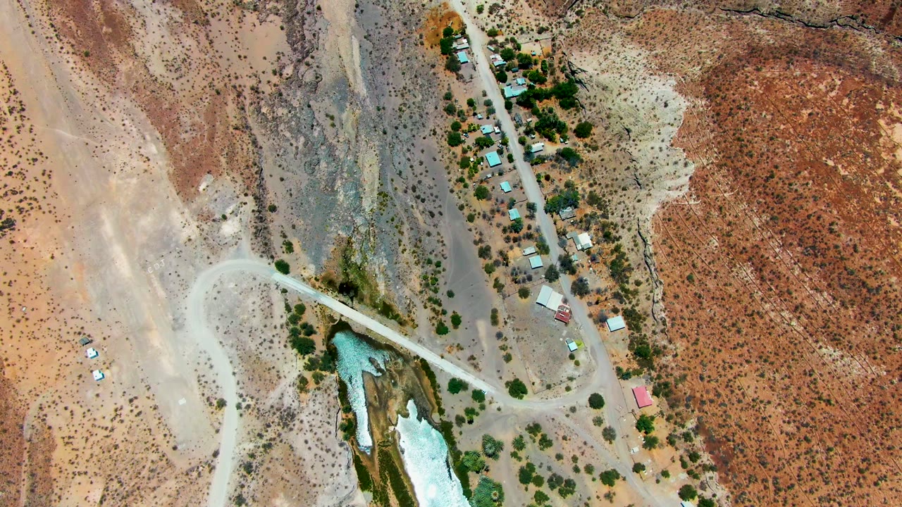 Aerial view of vehicles on a desert road near trees and small structures.