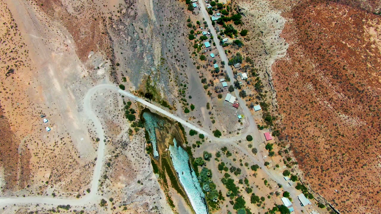 Aerial view of winding dirt roads, arid hills, water, and clustered buildings.