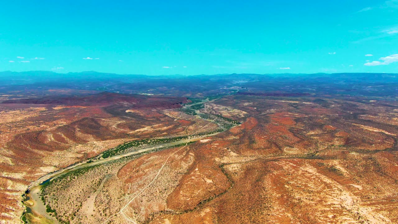 High desert aerial with river bend, road, and red-brown terrain.