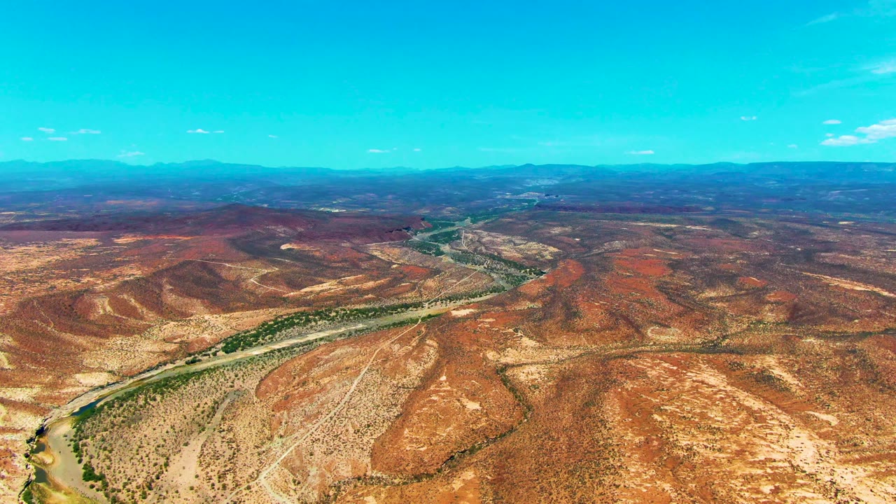 Dry red hills and a river channel seen from above with distant mountains.
