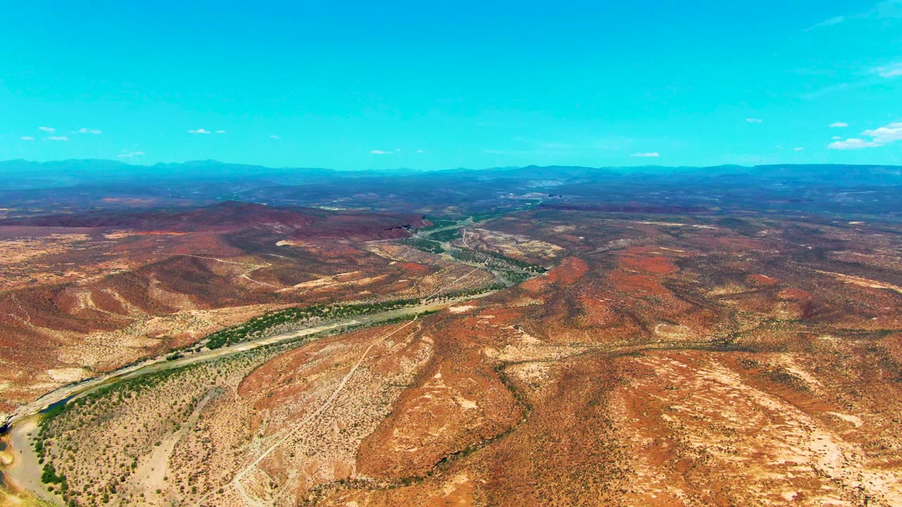 Wide aerial desert landscape with road and green wash crossing the hills.