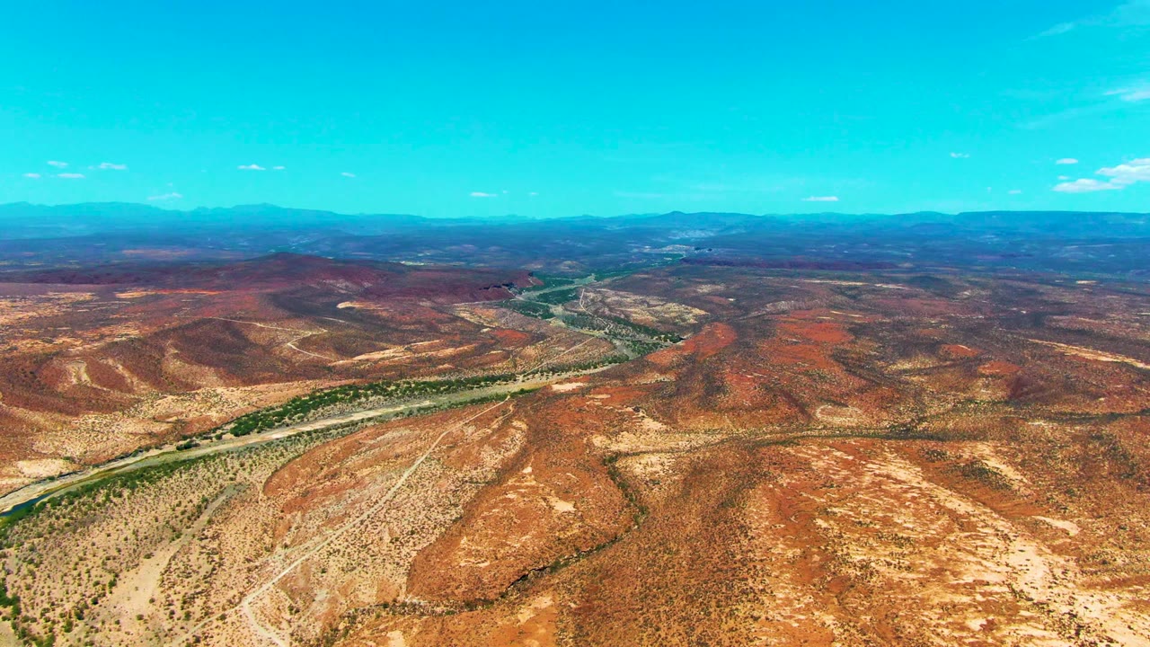 Wide aerial view of arid hills with a road following a green waterway