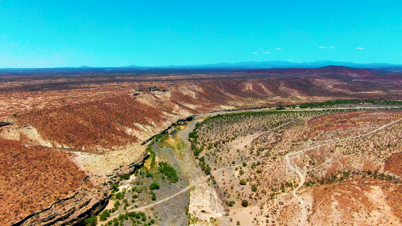 High view of a green-lined river channel crossing dry desert hills.