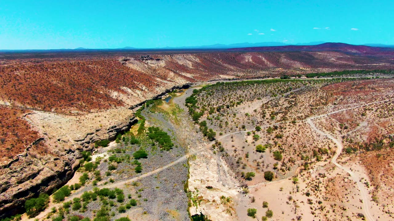 Wide aerial over a dry valley with river, scrub, and dirt road.