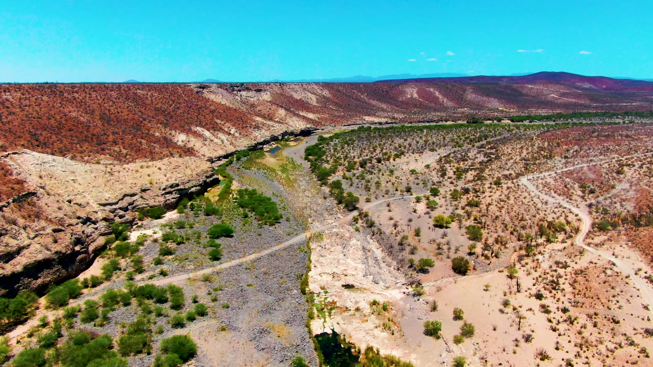 Wide aerial desert valley with a winding dirt road and dry wash.
