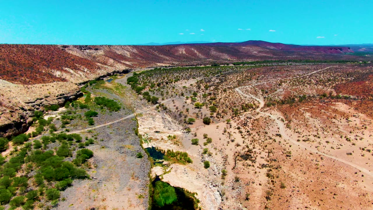 Aerial desert valley with a rocky riverbed, green vegetation, and low hills.