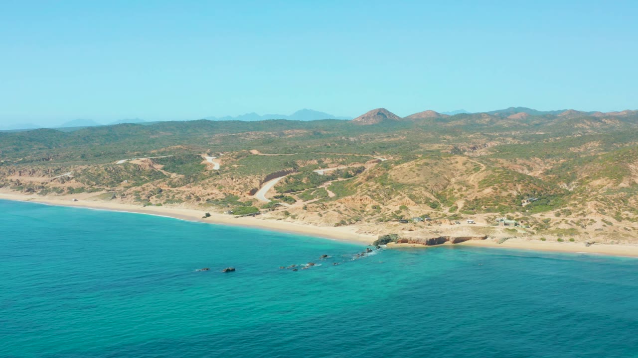 Wide aerial beach view with clear blue water and rolling inland hills