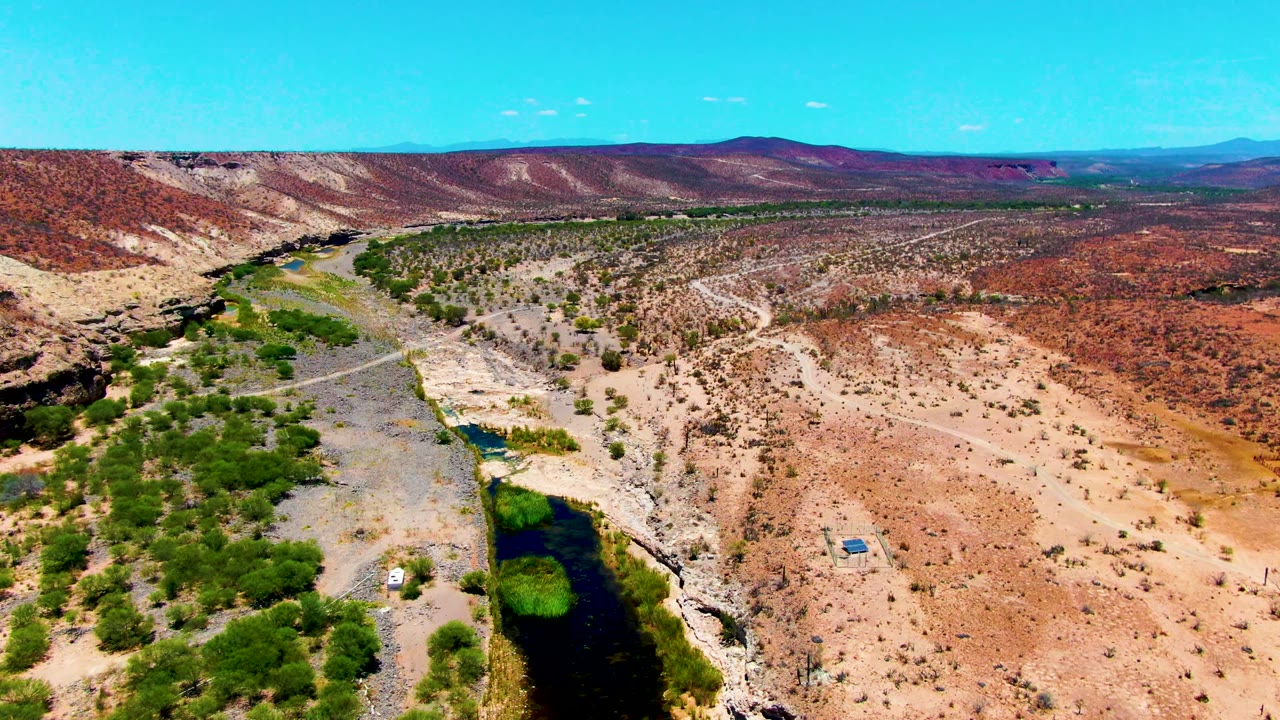 Drone view of a desert river corridor with green vegetation and dry roads.