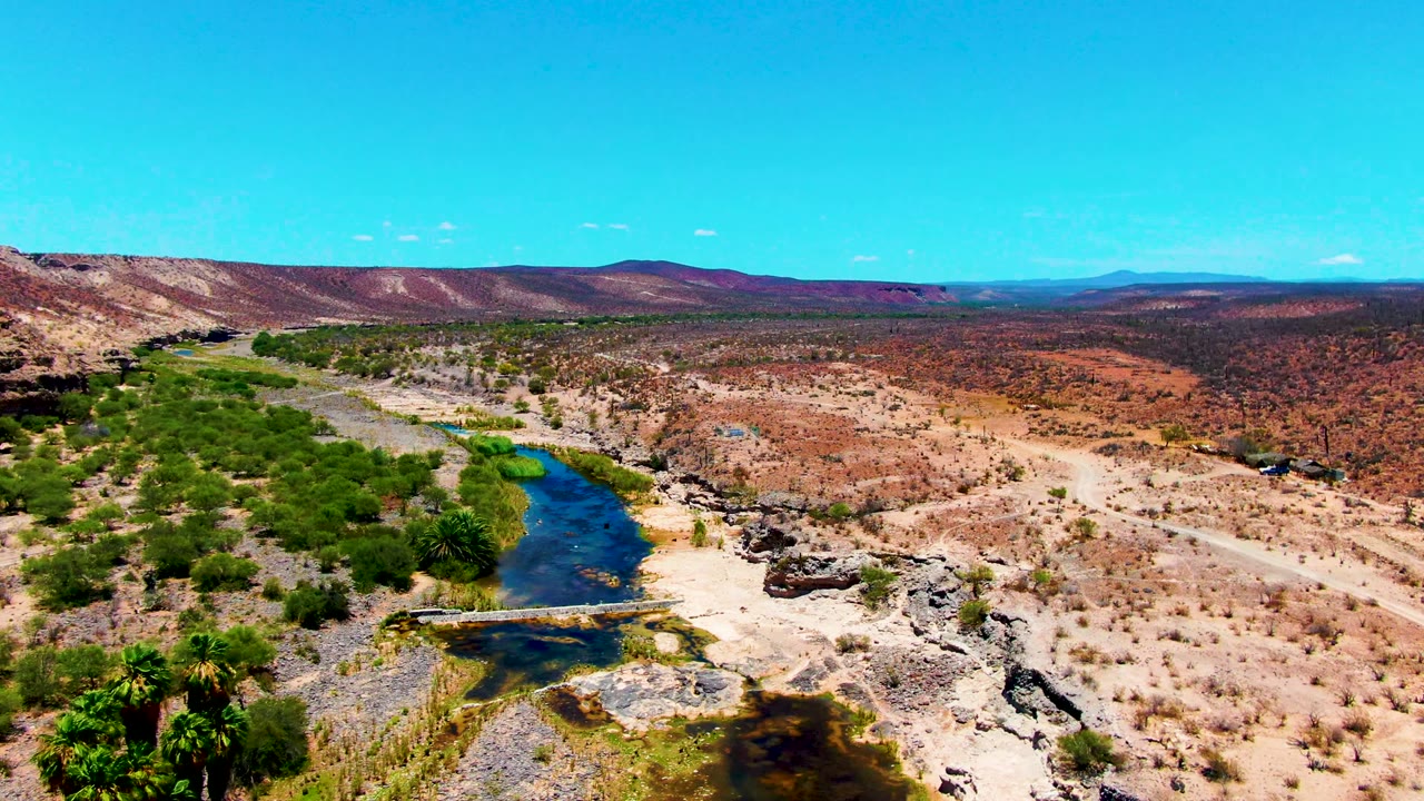 River and green trees in a rocky desert valley with hills on the horizon.