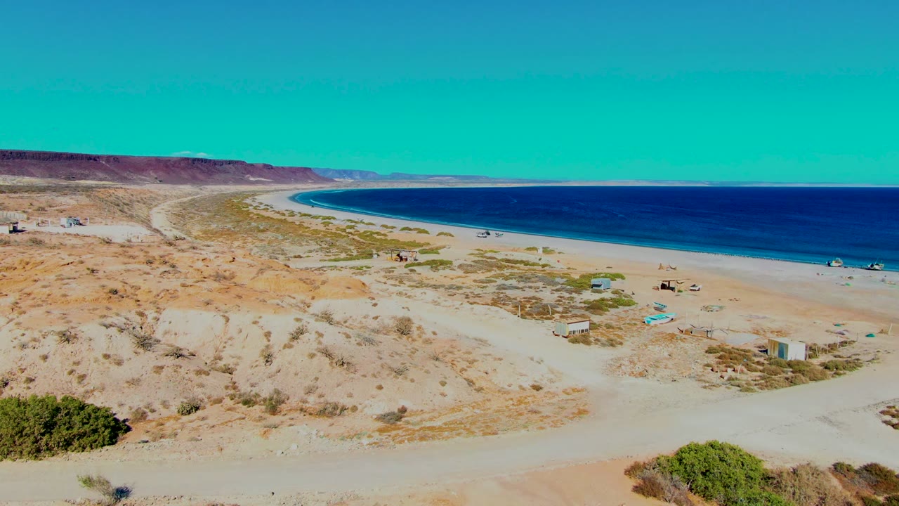 Desert foreground leading to a quiet beach and open ocean.