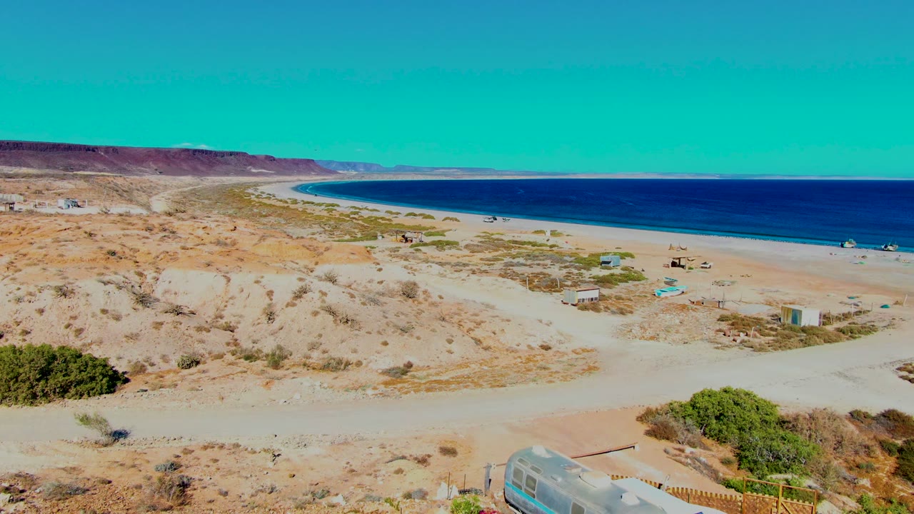Coastal dunes and ocean with small campsite structures in the distance.