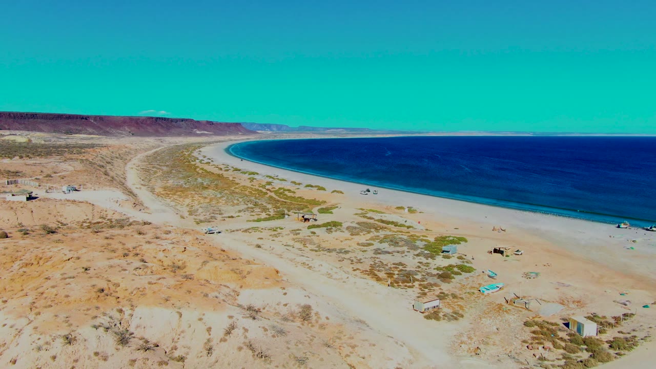 Curving beach and dirt road along arid shoreline.