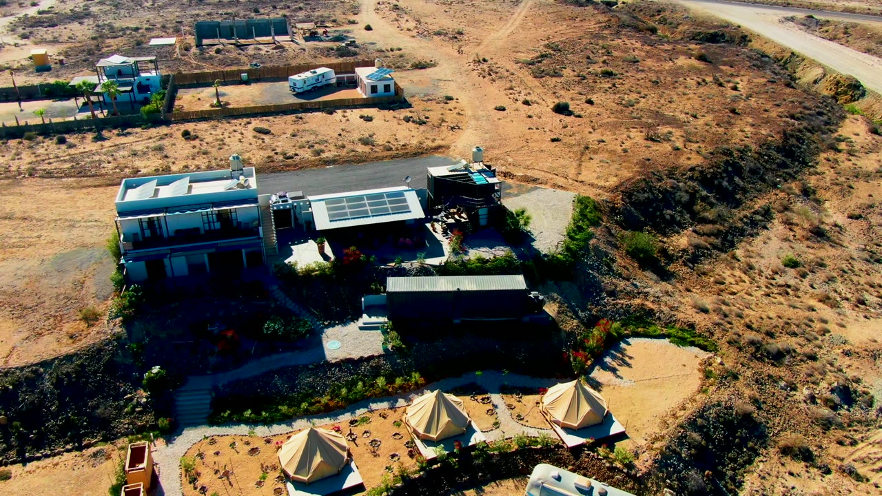 Drone view of van approaching buildings with solar panels and tents