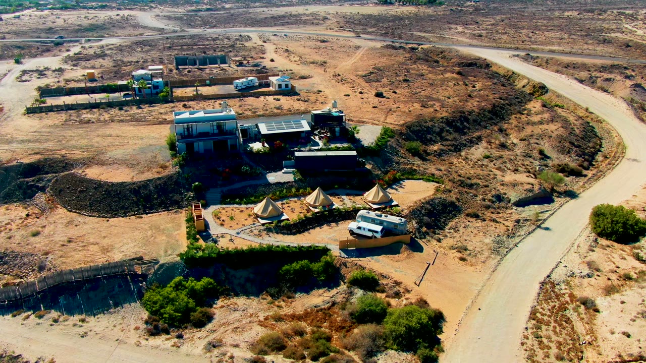 Overhead desert compound with tents, buildings, van, and road.