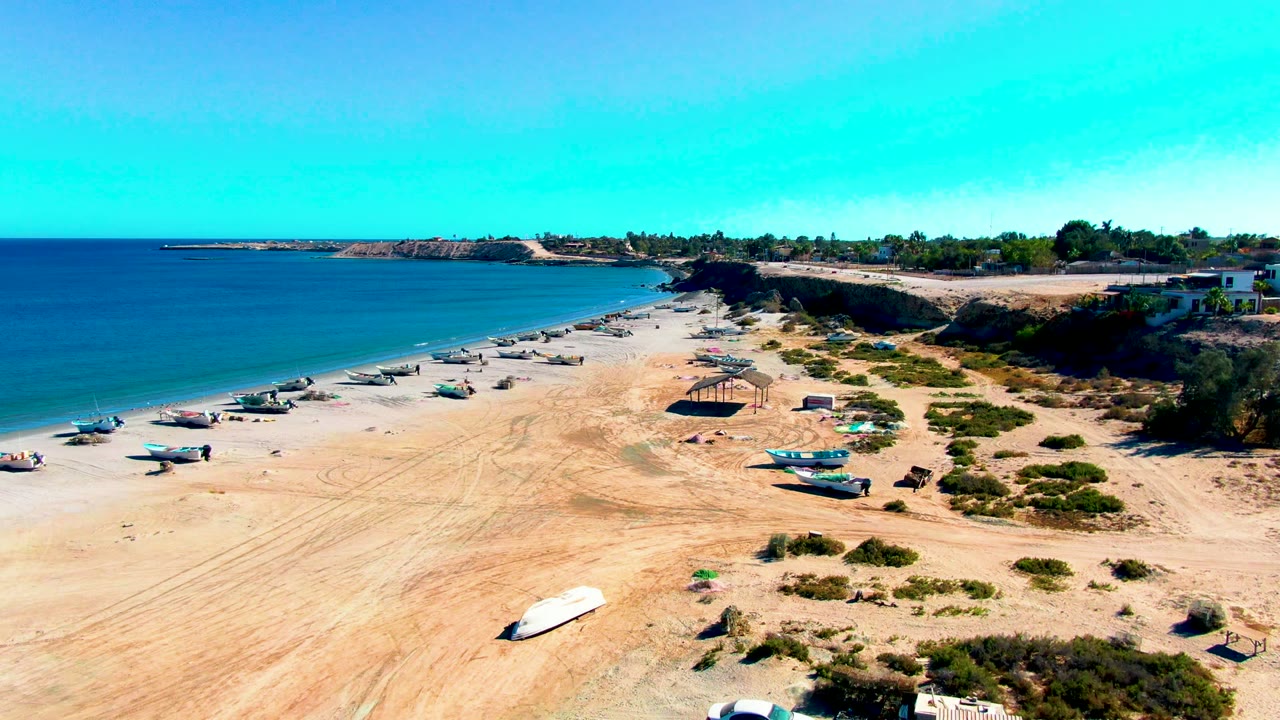 Wide beach aerial with boats on sand and calm ocean beside the shore.