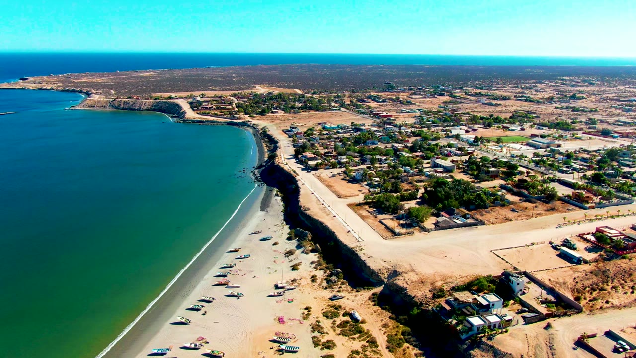 Drone view of ocean, beach, cliffside road, and inland town buildings.