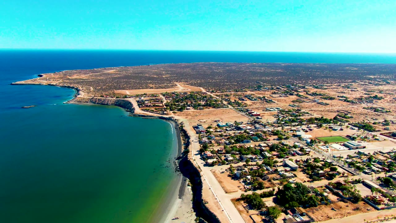 Drone view of ocean curving along a sandy beach and small settlement.