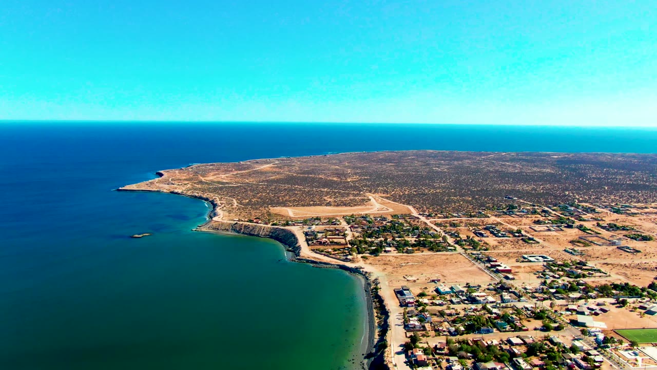 Third frame shows San Juanico from above, with green-blue water filling the left foreground, a pale beach and rocky curve along the coast, town buildings at lower right, and no visible people.