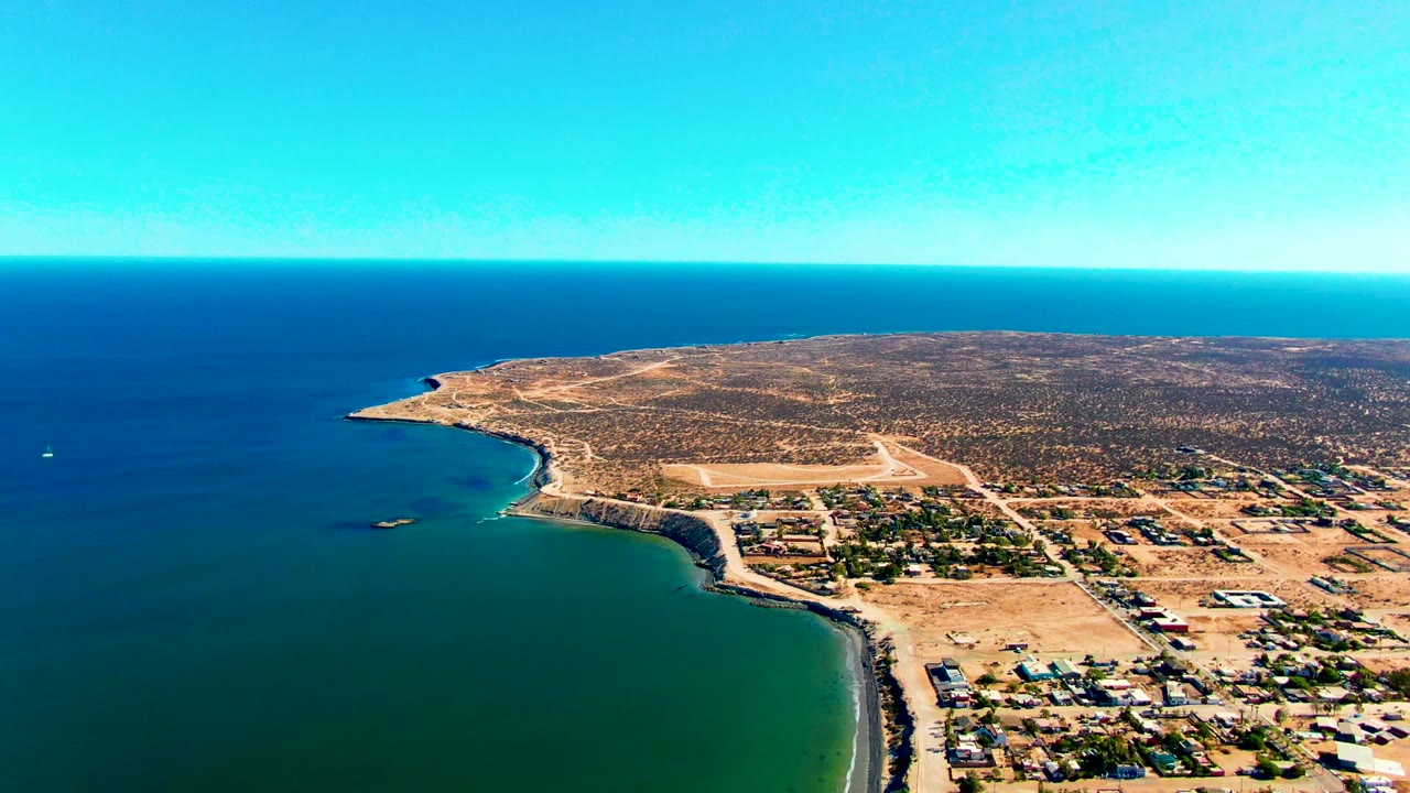 Wide drone view of coast, village roads, and blue ocean horizon.