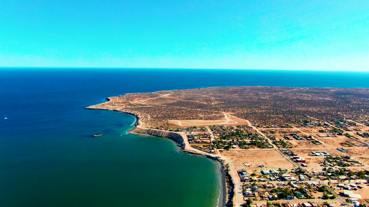 Aerial coastline with settlement, road, and open ocean.