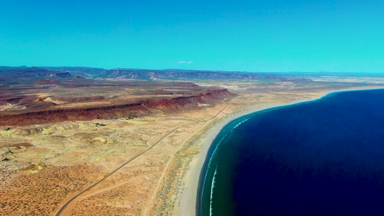 High aerial view of a dirt road, dry coastal plain, beach, and ocean.