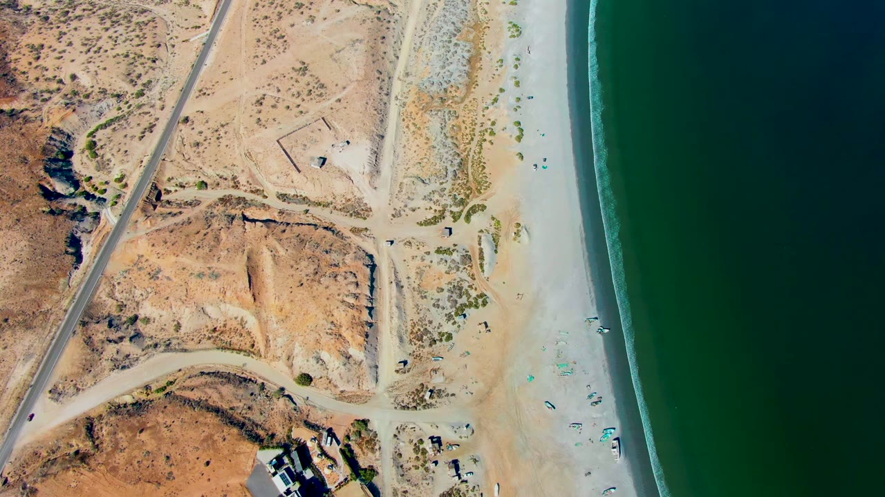 Drone view of sand, dunes, road, and ocean edge.