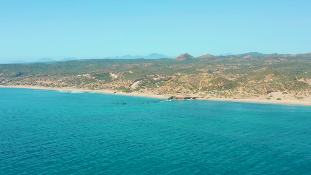 Wide aerial view of turquoise ocean beside a sandy Baja shoreline