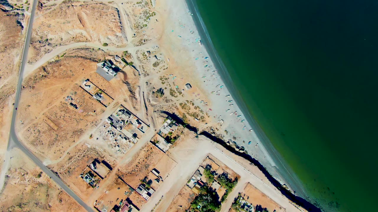 San Juanico aerial frame with the beach curving beside dark green water, roads and small buildings crossing the dry land, and no visible people.