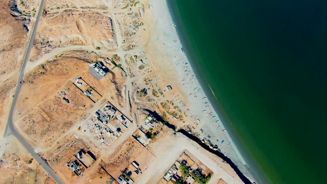 Aerial view of beach and coastal road beside scattered buildings.