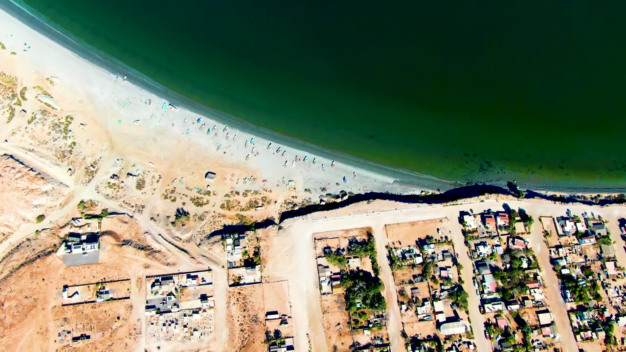 Aerial shoreline view with beachgoers along sand and homes below.