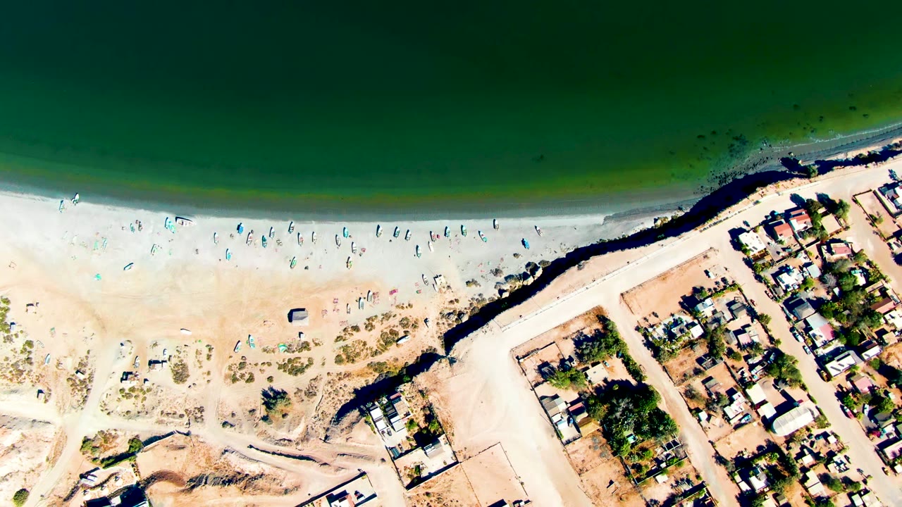 Overhead view of San Juanico beach in Baja California Sur, with dark green ocean above a pale sand shoreline and a residential block at the lower right.