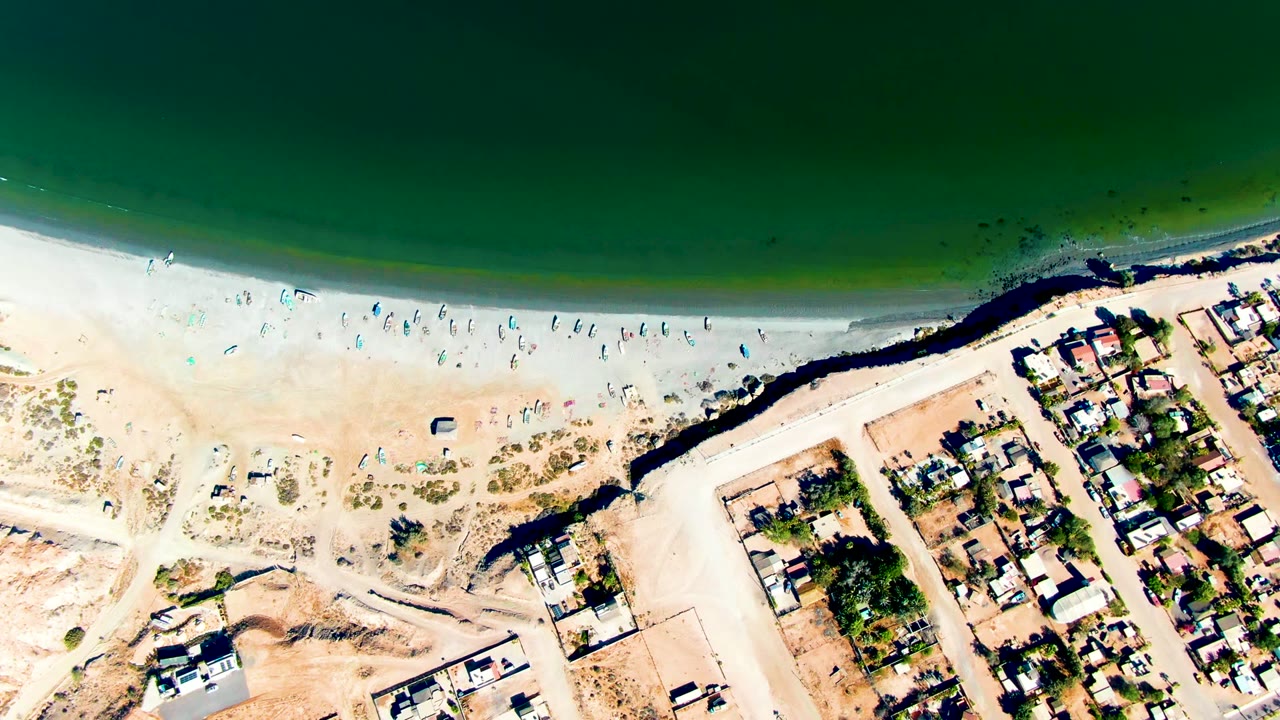 Aerial beach view with surf line, people, roads, and houses.