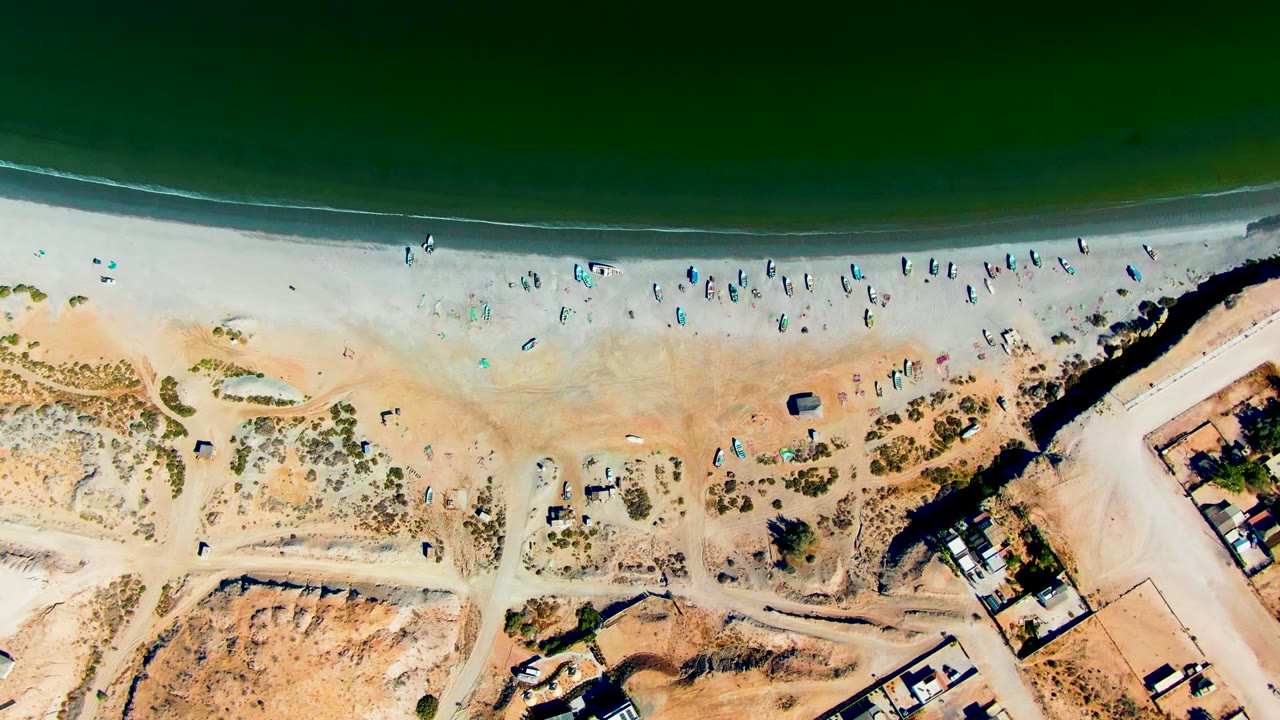 Aerial shoreline with beachgoers along the surf line and dry dunes below.