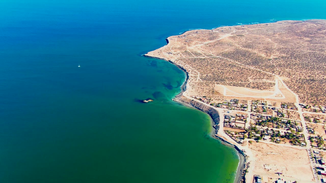 Clear coastal water with a small white boat and arid shore settlement below a desert headland.