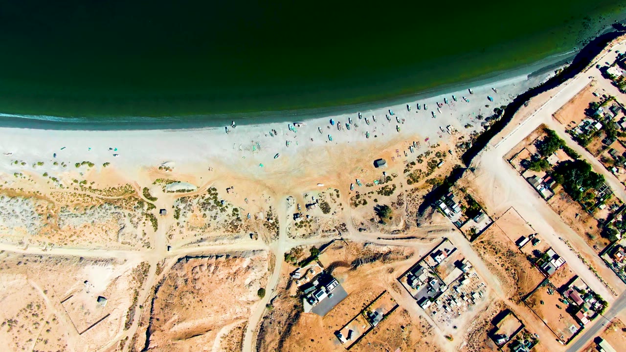 Aerial beach view with ocean, scattered people, roads, and homes.