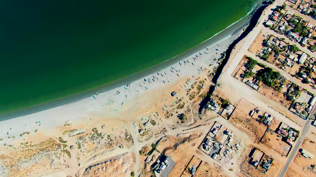 Aerial shoreline with beach umbrellas and residential streets beside the sand.