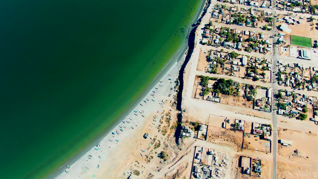 Aerial shoreline with boats on sand beside a residential grid.