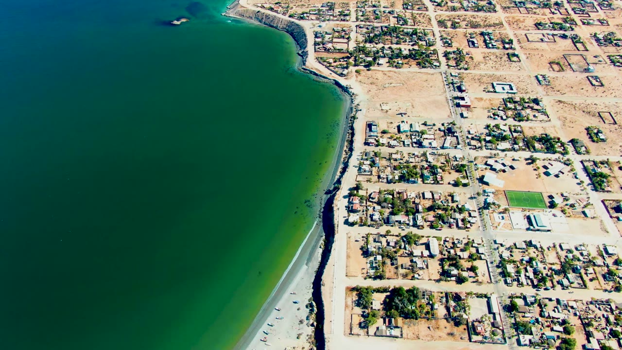 Drone view of shoreline, ocean, and coastal neighborhood with a small boat offshore.