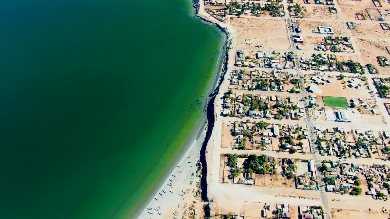 Overhead coastline with beach, homes, roads, and green water.