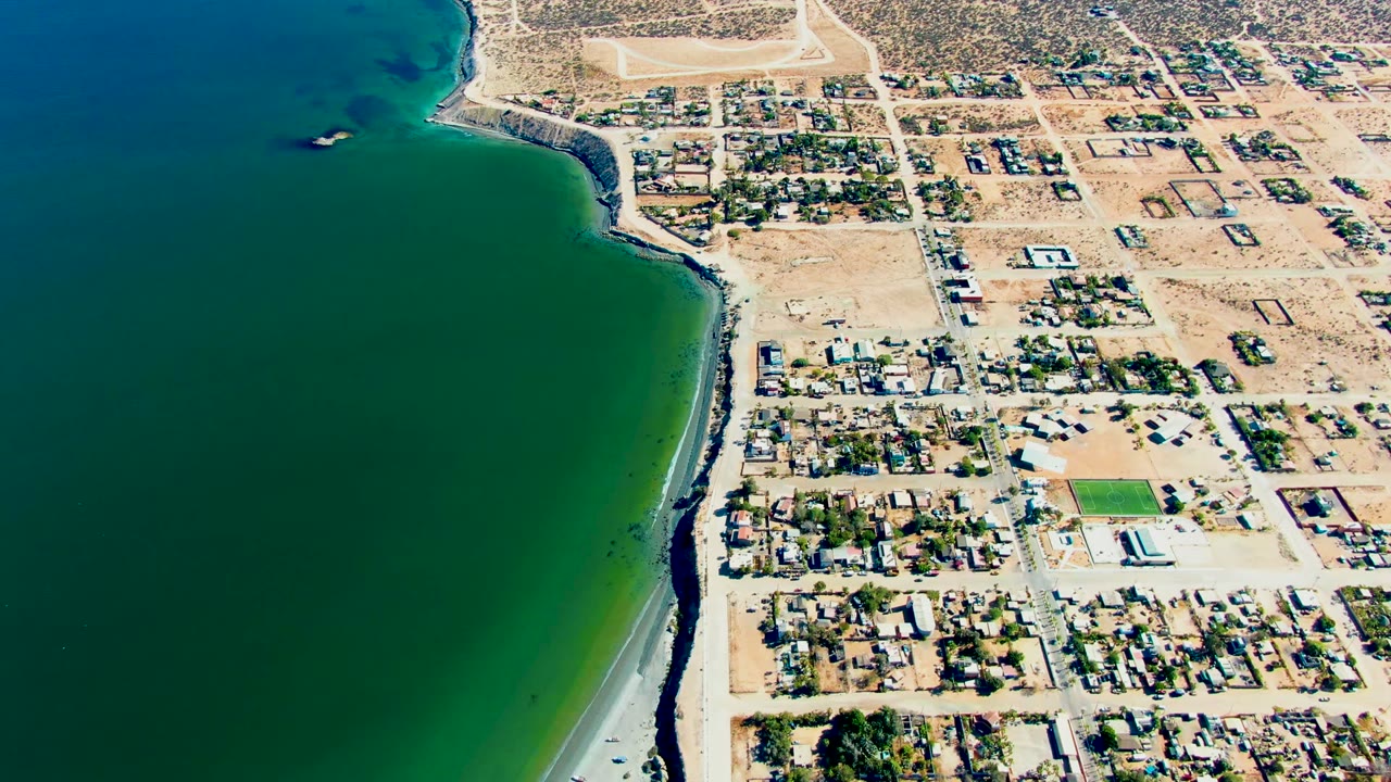 Coastal houses and roads beside green ocean water.