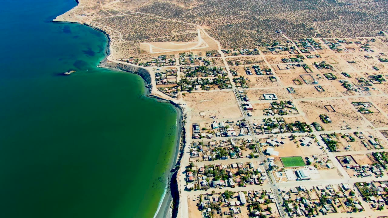 Aerial coastal town view with ocean, houses, street grid, and dry land.