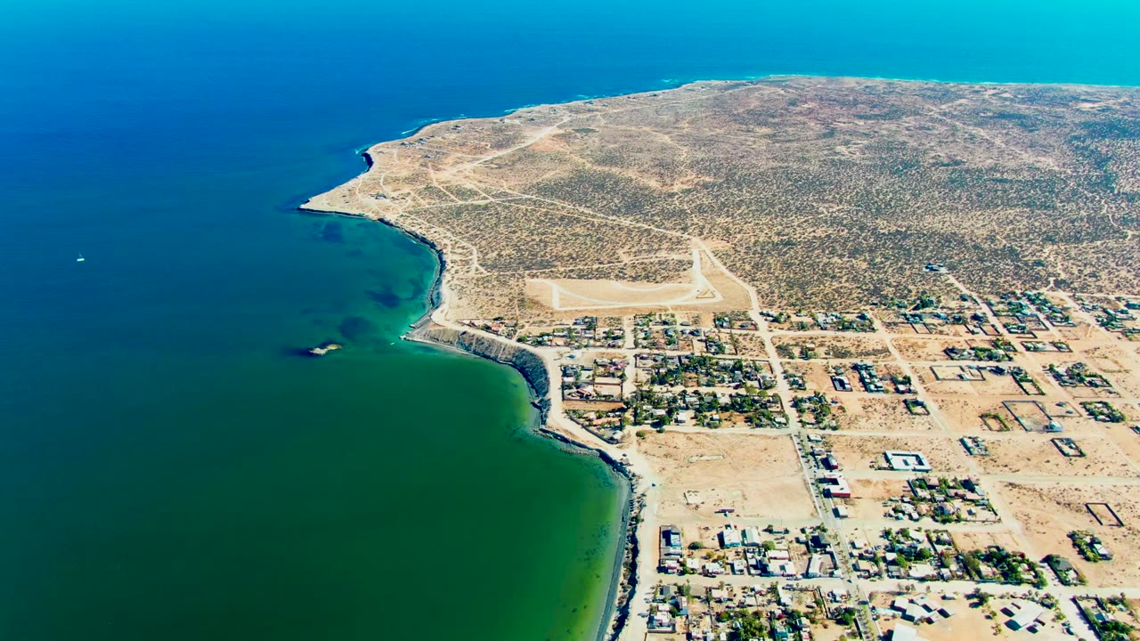 Coastal settlement beside green water with runway inland.