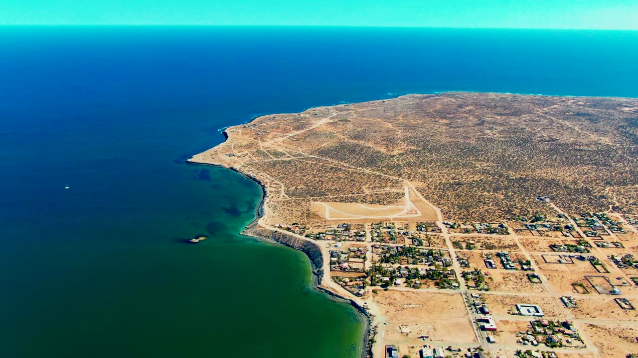 High aerial view of shoreline, small town blocks, and runway near the ocean.