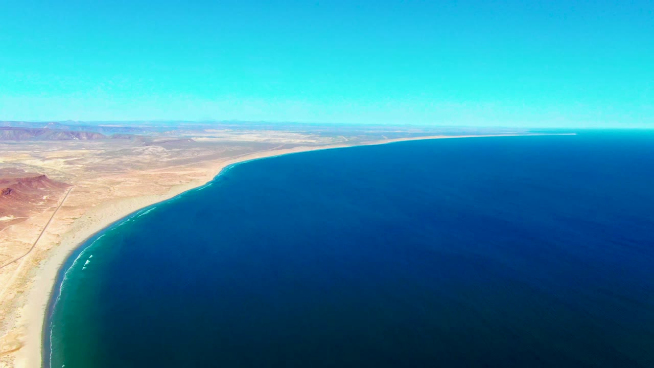 Curved sandy shore and calm ocean seen from high above.