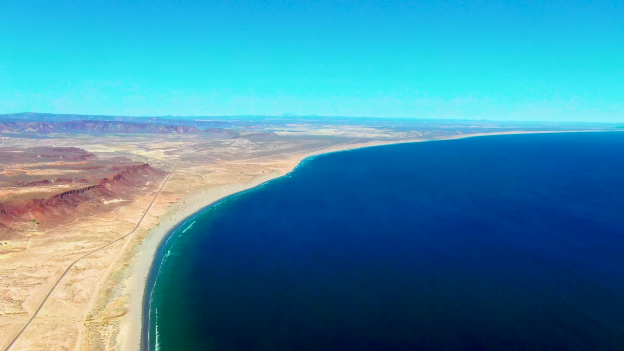 Curving sandy coast beside dark blue water and desert road